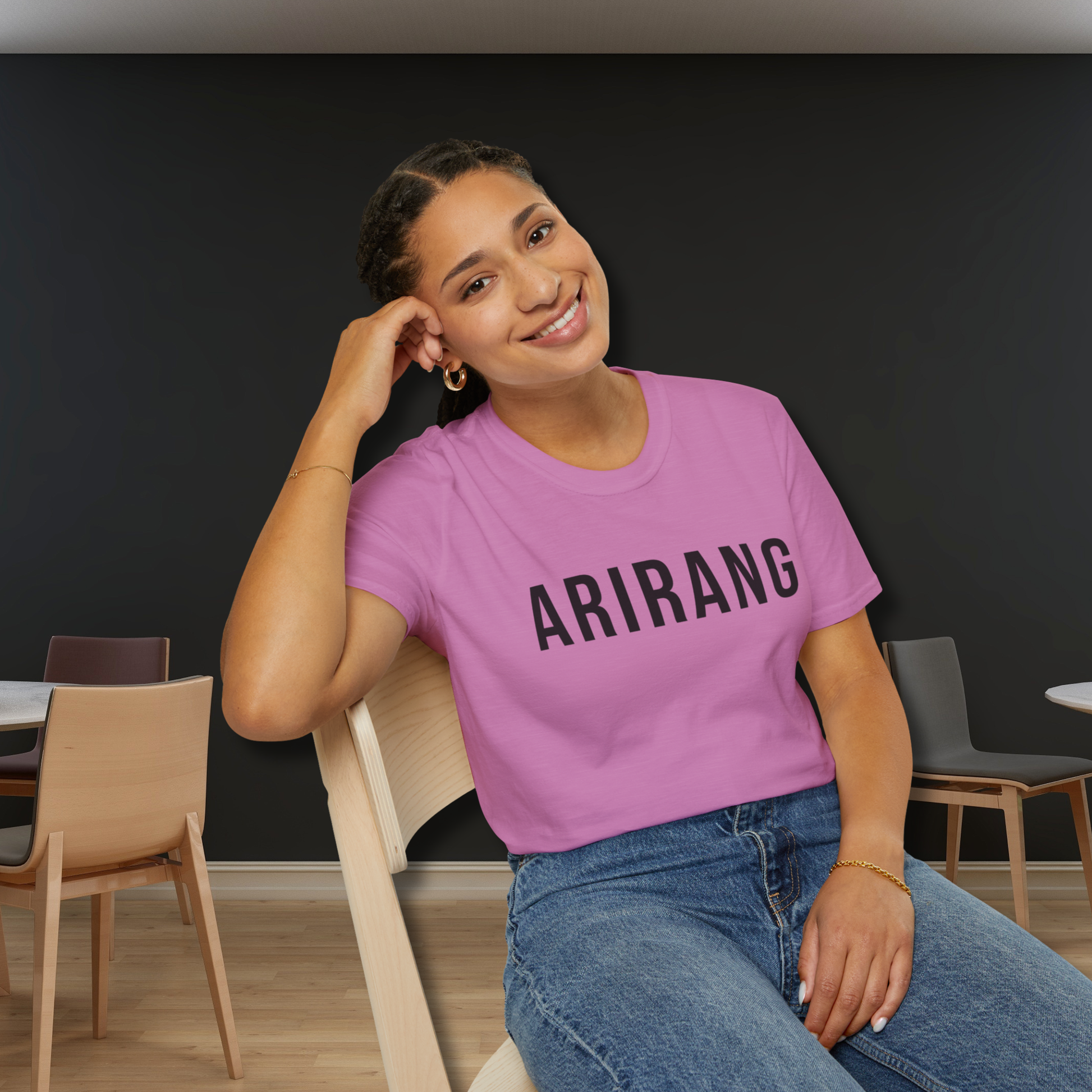 Person wearing a pink 'ARIRANG' t-shirt sitting in a room with chairs and tables. - Bangtan Tour 2026 Unofficial Shirt [Bias Arirang Color Vinyl Edition, Simple Text] - Jung Kook, JK, Orchid
