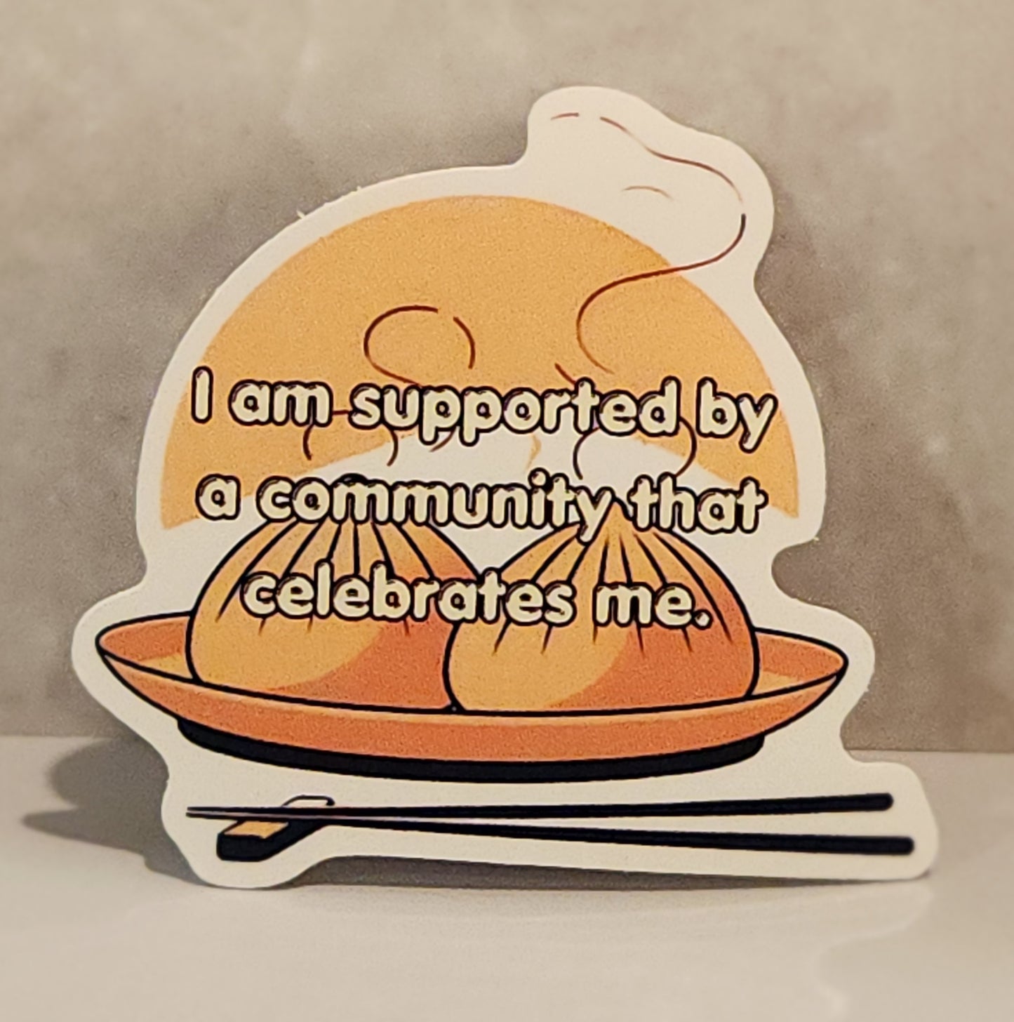 Sticker with dumplings and text 'I am supported by a community that celebrates me' on a beige - affirmation stickers - friends, zero oclock, yet to come, answer: love yourself, magic shopbackground