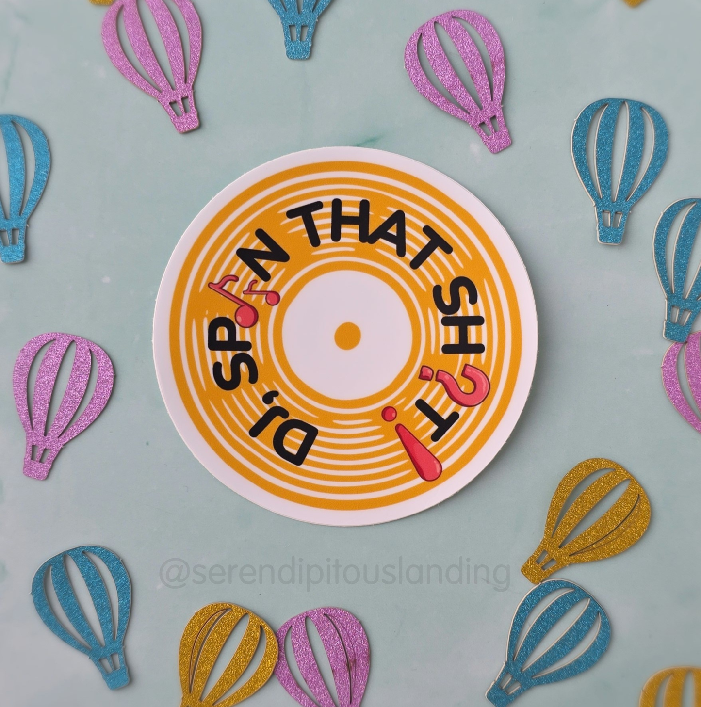 Circular sign with text surrounded by colorful hot air balloon cutouts on a light blue background - DJ Spin That Sticker | Serendipitous Landing