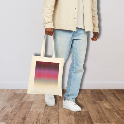 Person holding a tote bag with a colorful gradient design (inspired by the BTS Arirang vinyl colors) while standing on a wooden floor.