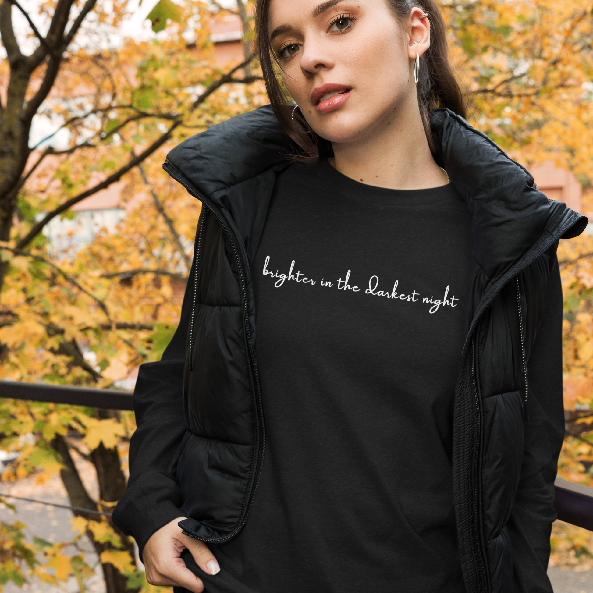 Woman wearing a black sweatshirt with text, standing outdoors with autumn foliage in the background. - The Insignia Bloom Long Sleeve Shirt (Unisex) - 7 Stars collection design - BTS / Bangtan members birth flowers and Arirang vinyl colors