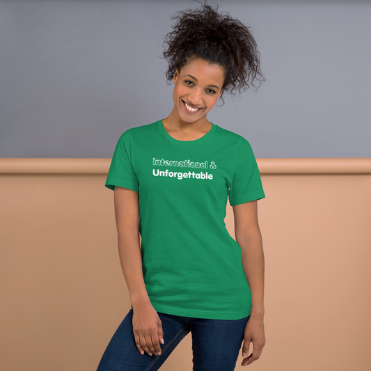 Woman wearing a green t-shirt with 'International & Unforgettable' text against a neutral background - Laureles Internacionales Unisex T-Shirt | Serendipitous Landing