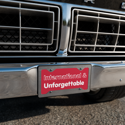 Car grill with a red license plate holder displaying 'International & Unforgettable'. - Laureles Internacionales Vanity License Plate - Serendipitous Landing